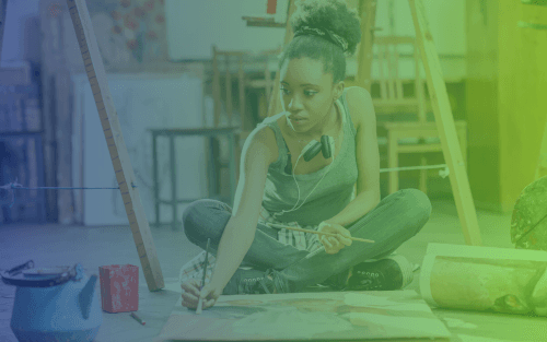 Student painting on the floor of an art studio, surrounded by supplies, expressing creativity through her artwork.